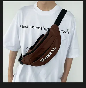 Detail of dark brown crossbody chest bag with TANBRNU logo on model wearing white t-shirt