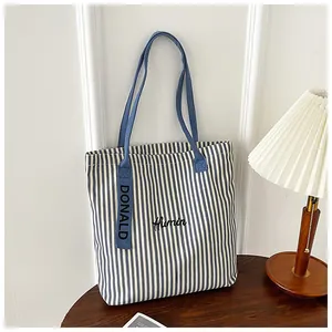 Close-up of blue and white striped canvas tote bag with Humin embroidery and woven label