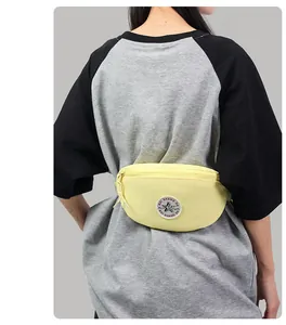 Detail of a light yellow nylon waist bag with a round logo patch worn by a model