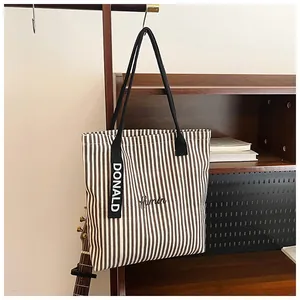 Detail of striped canvas tote bag with black strap handles and Donald tag hanging on a rack