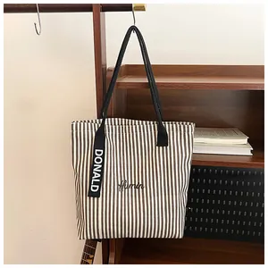 Detailed shot of striped canvas tote bag featuring Human embroidery and decorative strap
