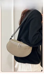 Khaki crescent saddle bag with dual silver zippers and adjustable black strap worn by model