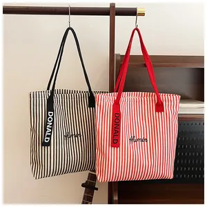 Detail of striped canvas tote bags with Humin embroidery and decorative logo ribbons