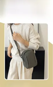 Deep green nylon crossbody bag shown worn by a model in a minimalist indoor setting
