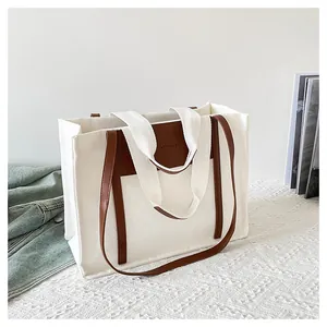 Detail of canvas tote bag with brown leather trim and fashion bag logo on white table