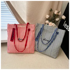 Detailed view of red and navy striped canvas tote bags with elegant cursive embroidery