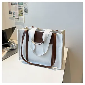 Close-up of white canvas tote bag featuring brown leather straps and fashion logo detail