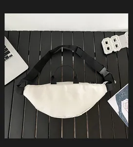 Flat lay of cream nylon chest bag with black adjustable strap on dark wooden desk