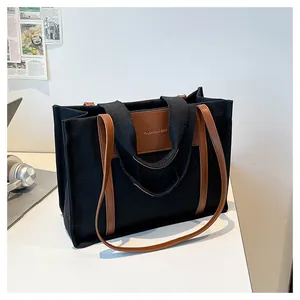 Detail of black canvas tote bag with brown leather handles and fashion bag logo label