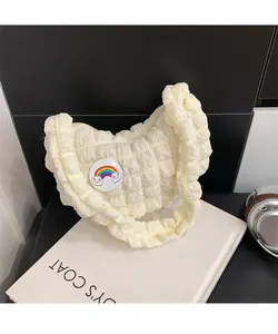 Gros plan du sac nuage plissé crème avec broche arc-en-ciel sur un livre blanc