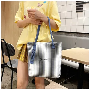 Detail of blue striped canvas tote bag featuring Humin embroidery and woven letter straps