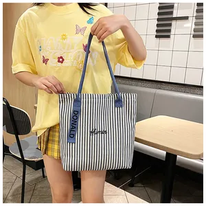Detail of blue and white striped canvas tote bag with embroidered logo and long strap
