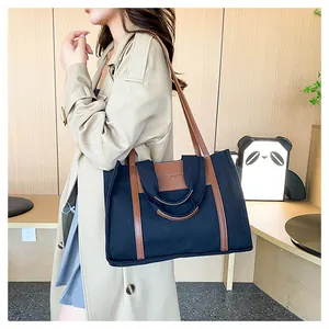 Detail of canvas tote bag with brown leather trim and shoulder strap on female model