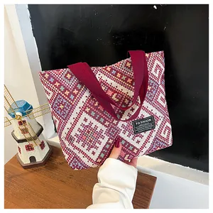 Close-up of geometric woven tote bag featuring red textile handles and fashion label