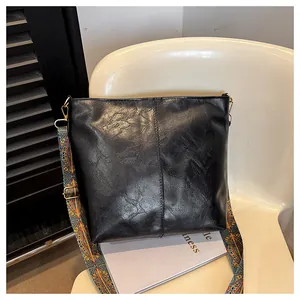Detail of black tote bag with vintage textured leather and colorful patterned strap
