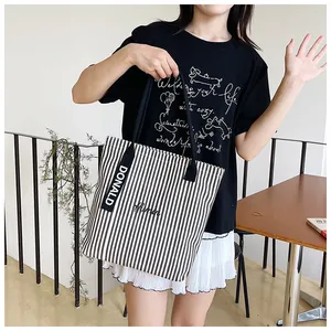 Detail of black and white striped canvas tote with embroidered script and wide shoulder strap