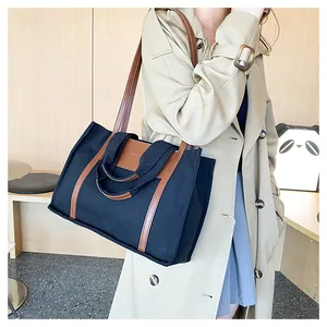 Detail of black canvas tote bag with brown leather straps shown on a model in a trench coat
