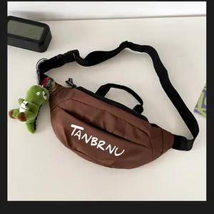Detail of coffee brown crossbody bag with logo and cute green dinosaur plush charm