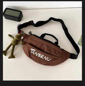 Brown sporty crossbody bag with white logo and a green plush bear charm on white desk