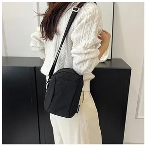 Close-up of black nylon crossbody bag showing the branded logo tag on a white sweater