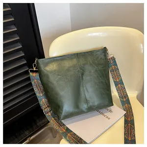Detail of deep green bucket bag featuring a textured leather finish and woven wide strap