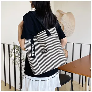 Detail of striped canvas tote bag showing Donald embroidery and wide black shoulder strap