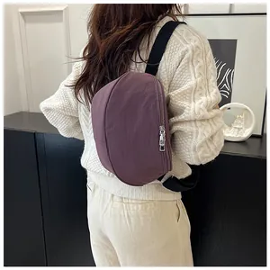 Detail of a purple crescent crossbody bag with black strap on a cable knit sweater