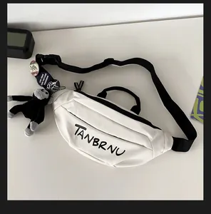 Close-up of white canvas chest bag with black zipper, TANBRNU text, and plush monkey charm