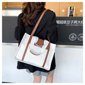 Back view of a model wearing a canvas tote bag with brown leather trim in a coffee shop