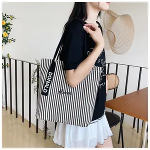 Detail of striped canvas tote bag with black strap featuring white DONALD embroidery lettering