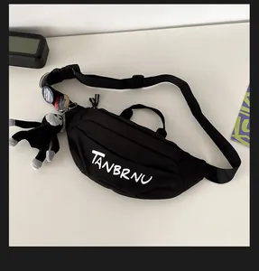 Detailed view of black nylon chest bag with white logo print and decorative plush charm