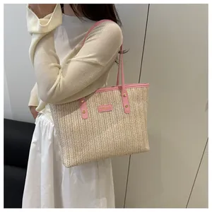 Detail of hand-woven beige straw tote bag with pink leather trim and brand logo tag