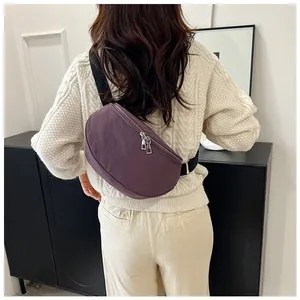 Purple nylon crescent crossbody bag with double zippers worn by a model in a casual setting