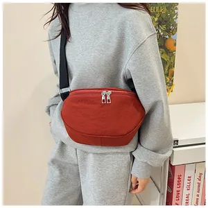 Detail view of brick red nylon crossbody saddle bag with adjustable black shoulder strap