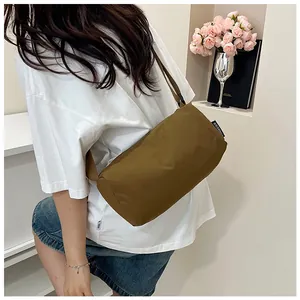 Close-up of brown nylon cylinder crossbody bag worn by a model in a minimal setting