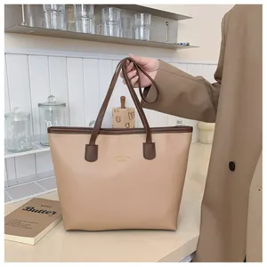 Detalle del bolso tote beige minimalista con bordes café oscuro y letras doradas moda