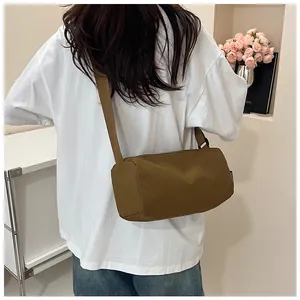 Brown nylon cylinder crossbody bag shown on a model with wide adjustable shoulder strap