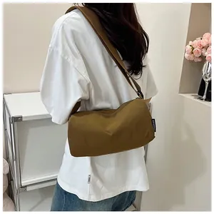 Brown nylon cylinder crossbody bag with shoulder strap worn by model in a minimalist setting