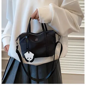 Model wearing a black nylon tote bag with a panda charm and adjustable strap