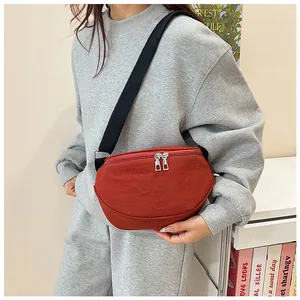 Close-up of a red canvas crescent crossbody bag with black adjustable strap and dual zippers