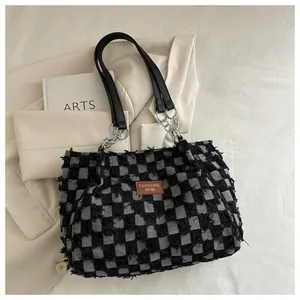 Détail d'un sac cabas en denim à carreaux avec bords effilochés et logo en cuir brun