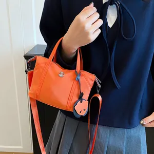 Vibrant orange nylon tote bag with bear charm and detachable shoulder strap in daily use