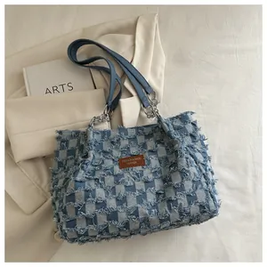 Détail du sac cabas en denim à carreaux avec bords effilochés et logo en cuir