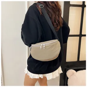 Detail view of khaki crescent sling bag with double zipper and wide black strap on model