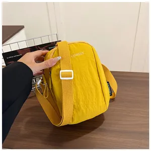 Detail of adjustable strap and white logo embroidery on yellow nylon crossbody bag