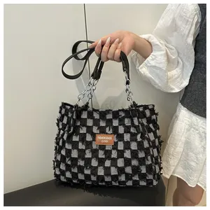 Gros plan du sac cabas en denim à damier avec bords effilochés et anses à chaîne argentée