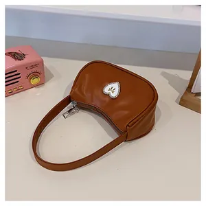 Nahaufnahme der braunen Halbmond-Handtasche mit Herz-Strass-Patch und goldenem Bogen