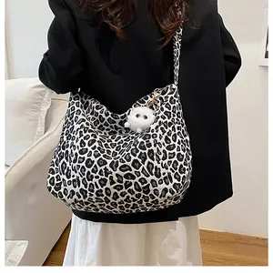 Détail du sac cabas en toile léopard avec un pendentif en peluche blanc sur un sac hobo