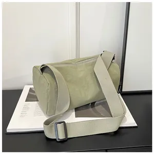 Detail of green nylon cylindrical crossbody bag showing micro-wrinkle texture and logo tag