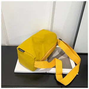 Detail of a bright yellow nylon cylinder bag with a side brand label and wide strap